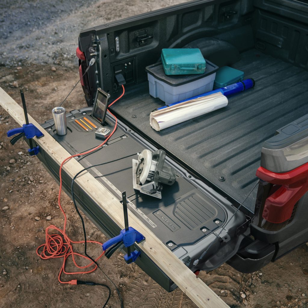 The tailgate of an electric F-150 Lightning being used to hold tools, cables, and a piece of wood.