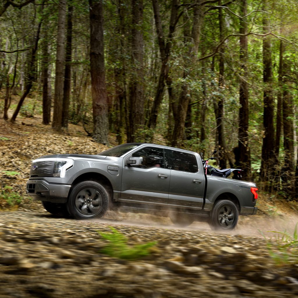 A 2022 Ford F-150 Lightning driving rapidly up a wooded mountain road in Edmond OK