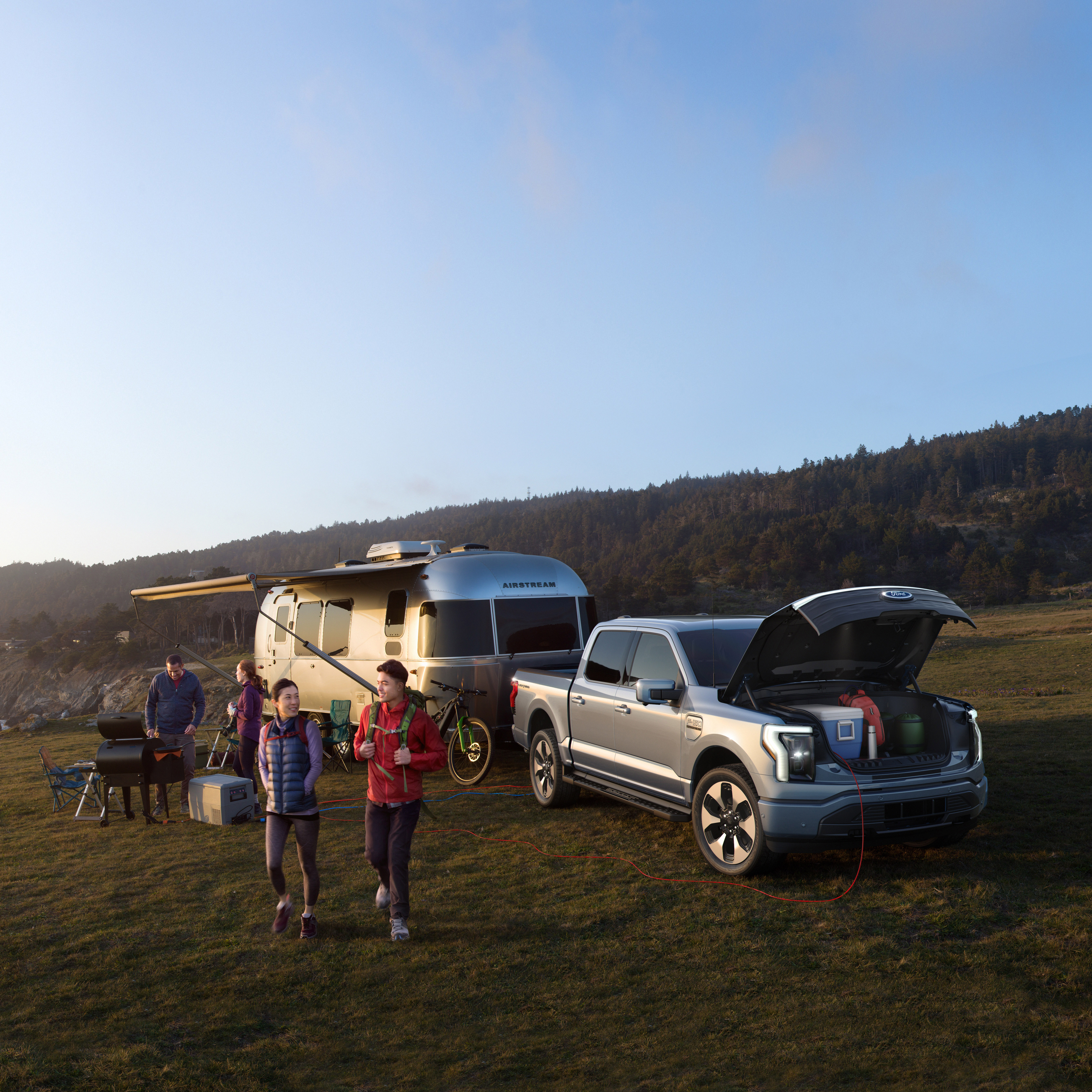 The new F-150 Lightning with the front trunk open at an outdoor campsite on a scenic hill.